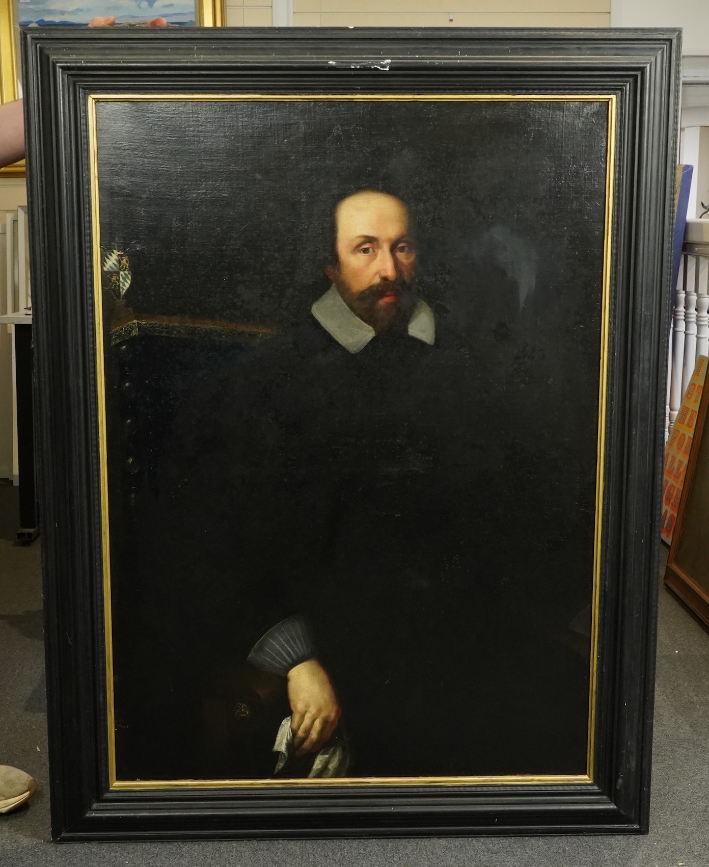 17th century Dutch School , Half length portrait of a seated gentleman, an armorial beyond, oil on canvas, 113 x 81cm